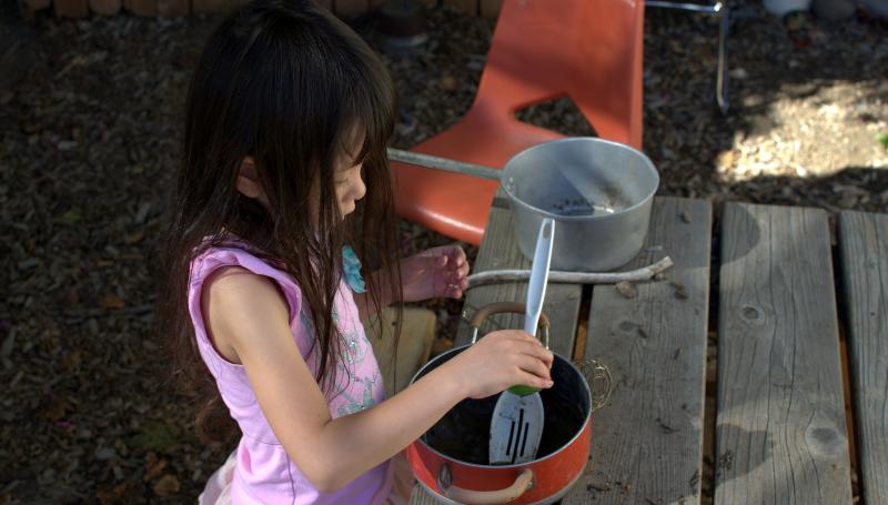 child playing outside in the dirt with pots.