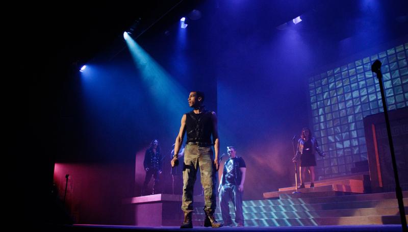 Under dramatic stage lighting, an actor gazes out into the crowd