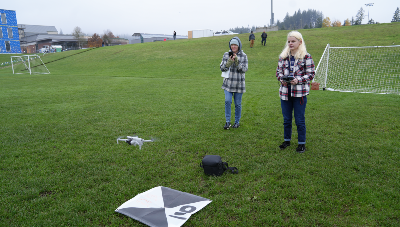two students launching a drone on the LCC soccer field