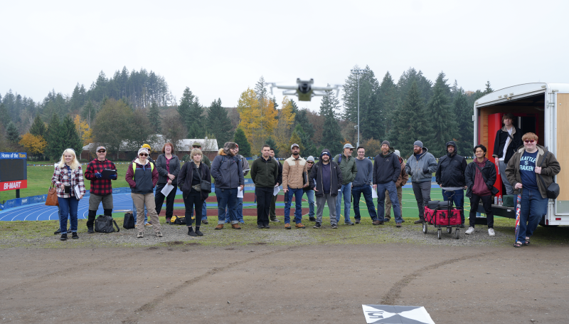a whole class of UAS students posing with a flying drone in the foreground