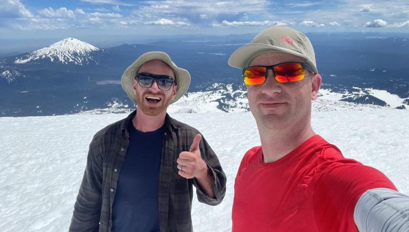 ESL instructor Kurtis Foster and web developr Kyle Schmidt smiling at the peak of a snowy mountain in the Oregon cascades