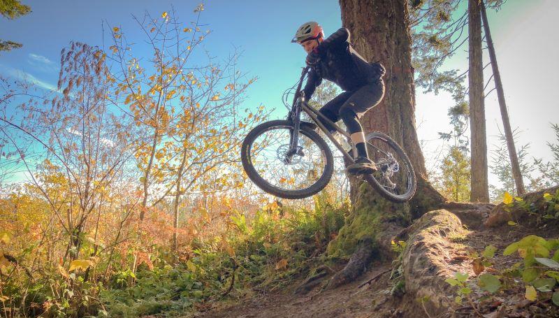 LCC employee Josh Taylor making a killer jump on a mountain bike in an bright, autumy forest