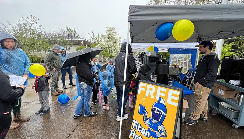 a group of people in raincoats lining up to get hot chocolate at the LCC open house