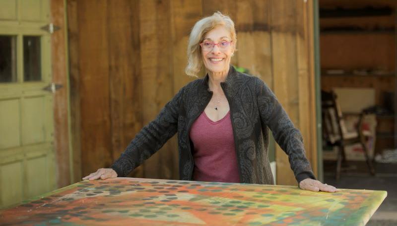 artist Kathleen Caprario, a fashionable older woman, posing with one of her artworks in a wooden barn