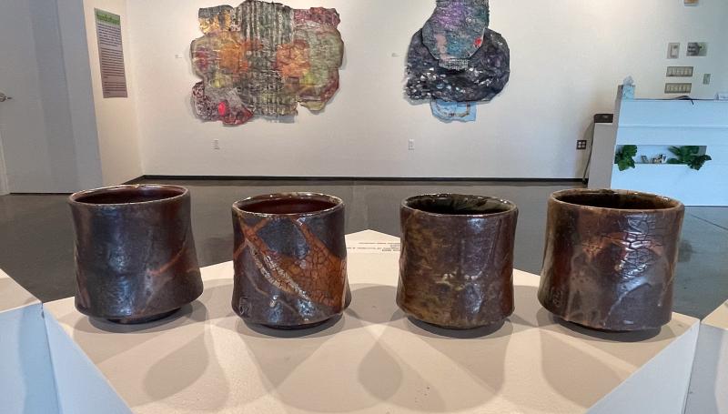 Coppery ceramic cups by Joe Geil and abstract pastel artworks Erin Langley in a gallery