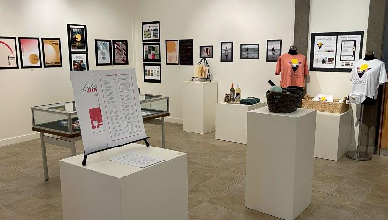 a bright art gallery room filled with graphic design student work including posters, shirts, and products