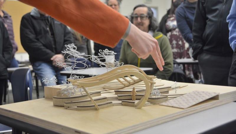 A student shows off an amphitheater model to a crowded room of onlookers