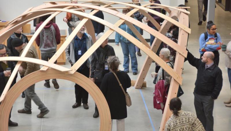 members of the LCC community examine a wooden gridshell shelter designed for campus grounds
