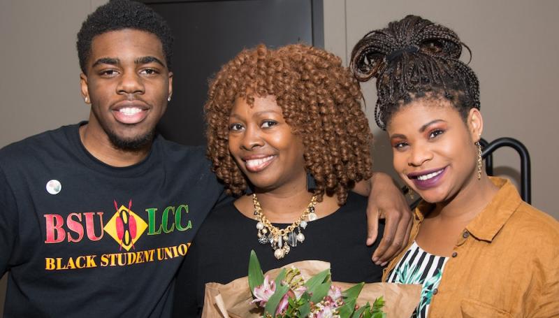 two African American students, a young man and a woman, pose with a guest speaker who holds flowers