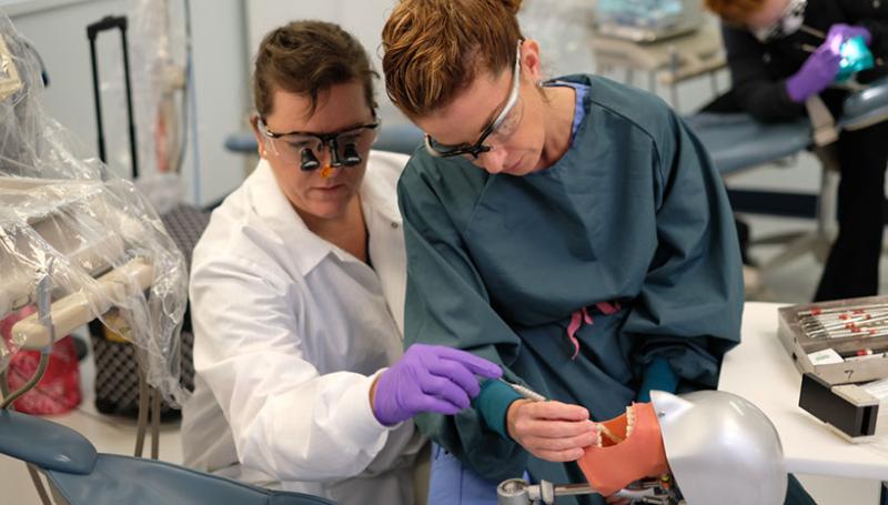 A woman working with her instructor on a mannequin's teeth