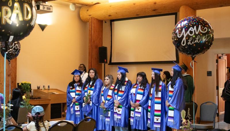 7 mecha students in blue caps and gowns and serape stoles happily celebrate their graduation at the Longhouse