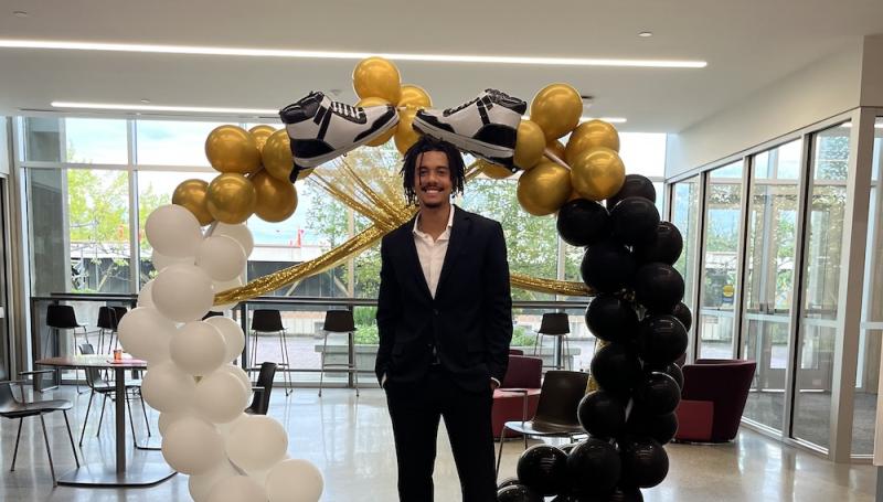 an African American young man in a suit and sneakers poses by a ballon arch at the BSU sneaker ball