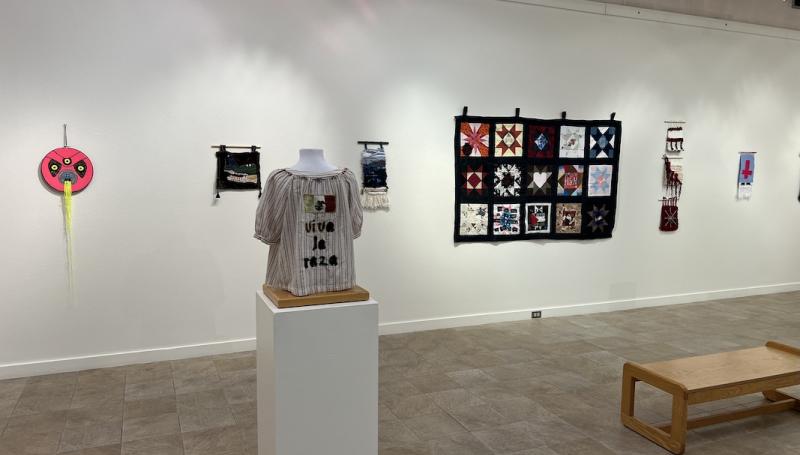 an art gallery with student fiber art pieces, including a shirt that says "viva la raza"