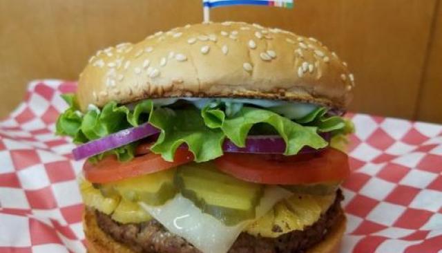A photograph of a burger with lettuce, onion, tomato and pickles.