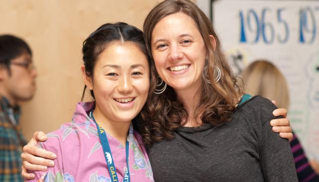 Two student friends, a young Asian woman and a young white woman, smile and pose together closely
