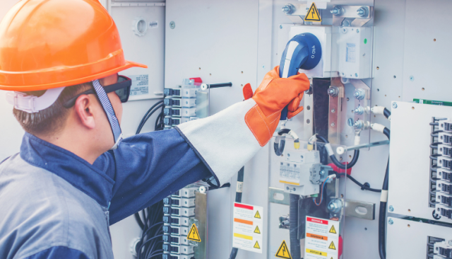 an electrician with a safety helmet and thick gloves does industrial repair