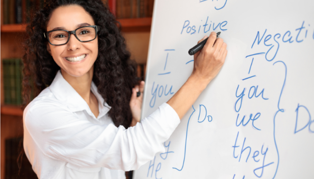 Smiling teacher points to English word conjugations