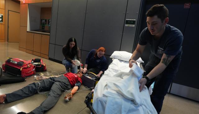 emt students practicing by moving a dummy to a gurney