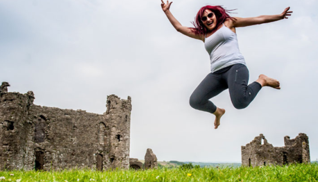 a student playfully jumps in a field in front of castle ruins