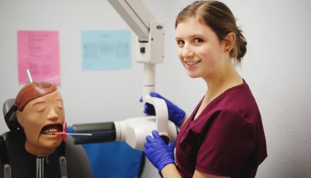 A student practices doing an x-ray with on a mannequin at dental assisting school 