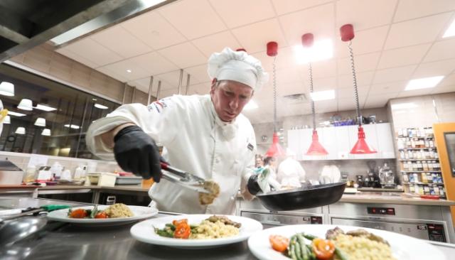 A culinary school student in chef uniform plating food in the kitchen