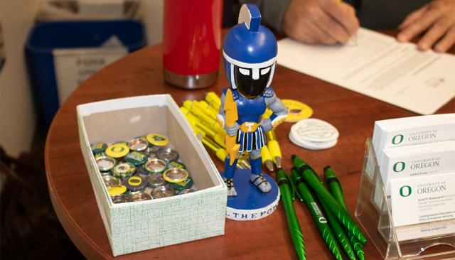 bobblehead lane mascot ty on a desk with university of oregon branded pins, pens and business cards
