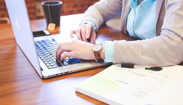 A BSN student in a cardigan studies nursing at a laptop with a textbook and a cup of tea