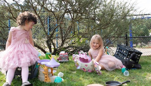 two little girls in pink dresses smile and laugh as they play in the Lane Child and Family Center playground
