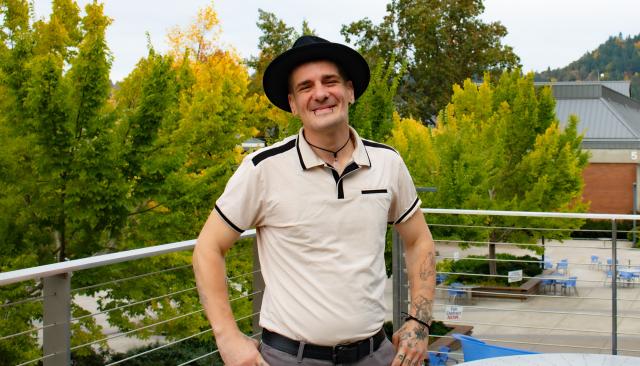 Wildland Fire Management student Cameron Stoker, a man in his 30s with a warm smile, tattoos, piercings, and stylish wide-brim hat posing by trees