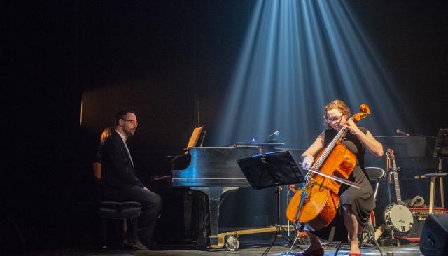Person playing a cello on dark stage with spotlight