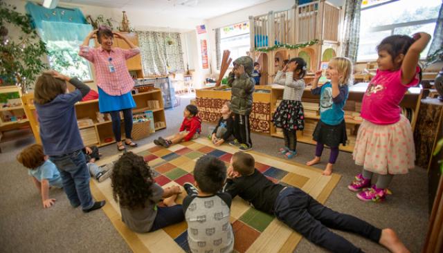 a smiling Lane Child and Family Center employee leads children in an activity in a sunny room filled with educational toys