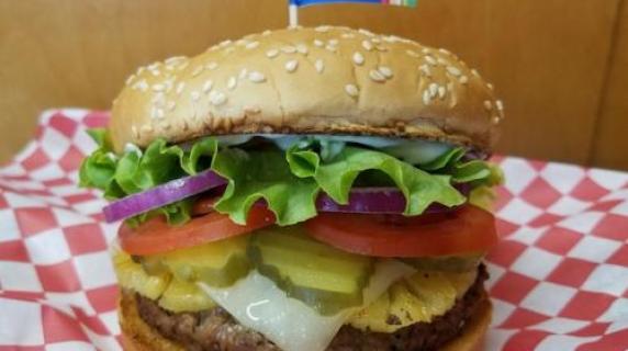 A photograph of a burger with lettuce, onion, tomato and pickles.
