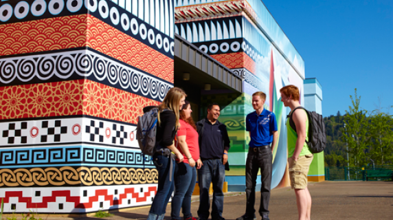 Five students standing together outside on a bright day