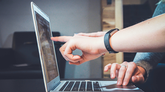 two students collaborate on an assignment, one points to a laptop