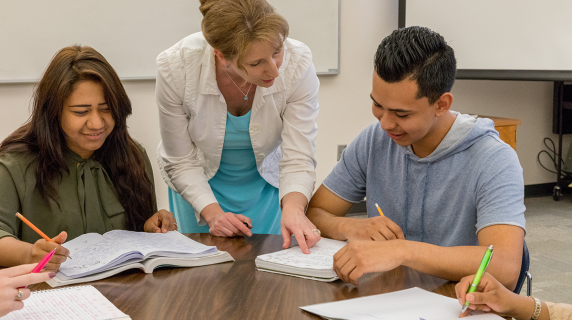 A friendly instructor helps students with their work in a bright classroom