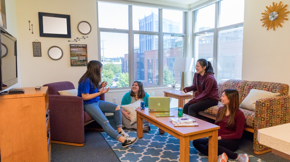 International Students, four young women, hang out on a couch in a sunny, spacious apartment