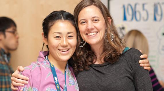 Two student friends, a young Asian woman and a young white woman, smile and pose together closely