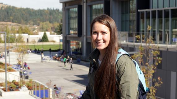 A young woman with a backpack smiling in front of Center Building on main campus
