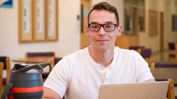 a scholarship winner, a young manwith glasses, working on a laptop