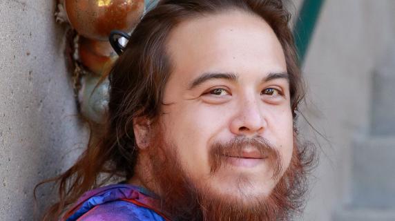 A student with a beard, long hair, and a tie-dye shirt