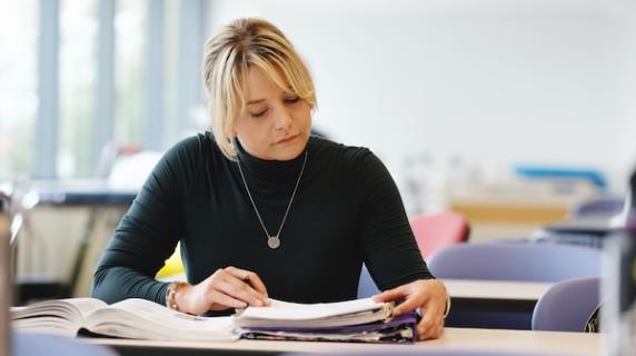 a student, a young woman, sits at a desk and studies in a bright room