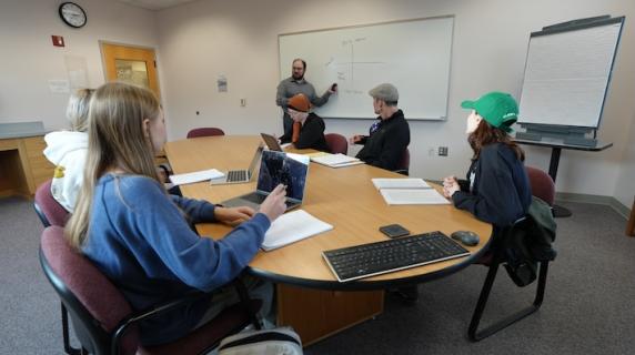 a business instructor, a friendly man with a beard, teaches a small business class in a conference room