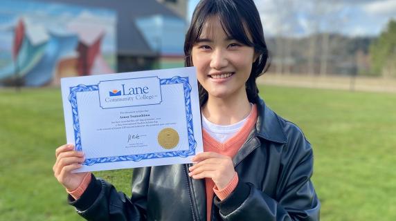 An international student, a young Japanese woman, smiles and shows off her LCC degree