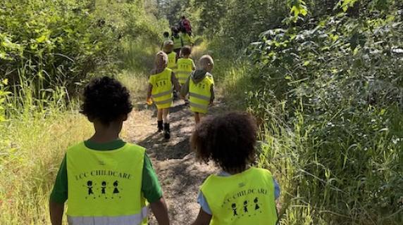 preschoolers with safety vests walks hand in hand down a nature path on a beautiful summer day