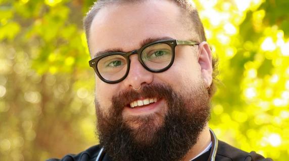 A man with a beard and a stethoscope wearing scrubs 