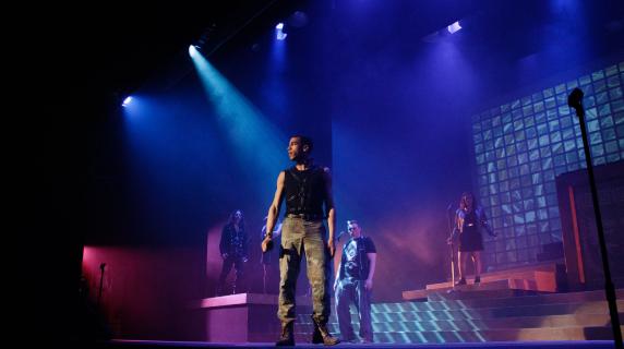 Under dramatic stage lighting, an actor gazes out into the crowd