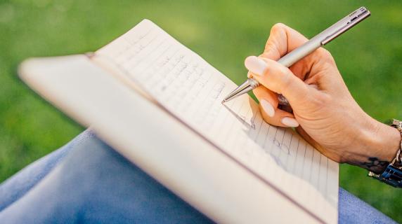 person writing on notepad propped up on their knees