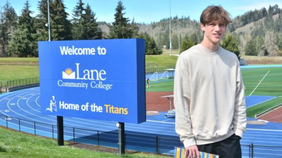 a high school student on a campus tour poses in front of our track with forest and hills in the background