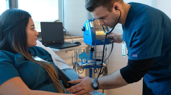 two bachelor of science in nursing students, one male and one female, practice taking blood pressure in the LCC nursing clinic