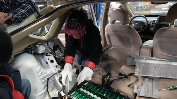 A high schooler with pink dyed hair repairs a car at automotive summer camp